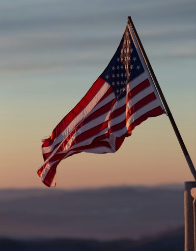 A vibrant US flag waves against a scenic sunset backdrop in Stowe, Vermont.
